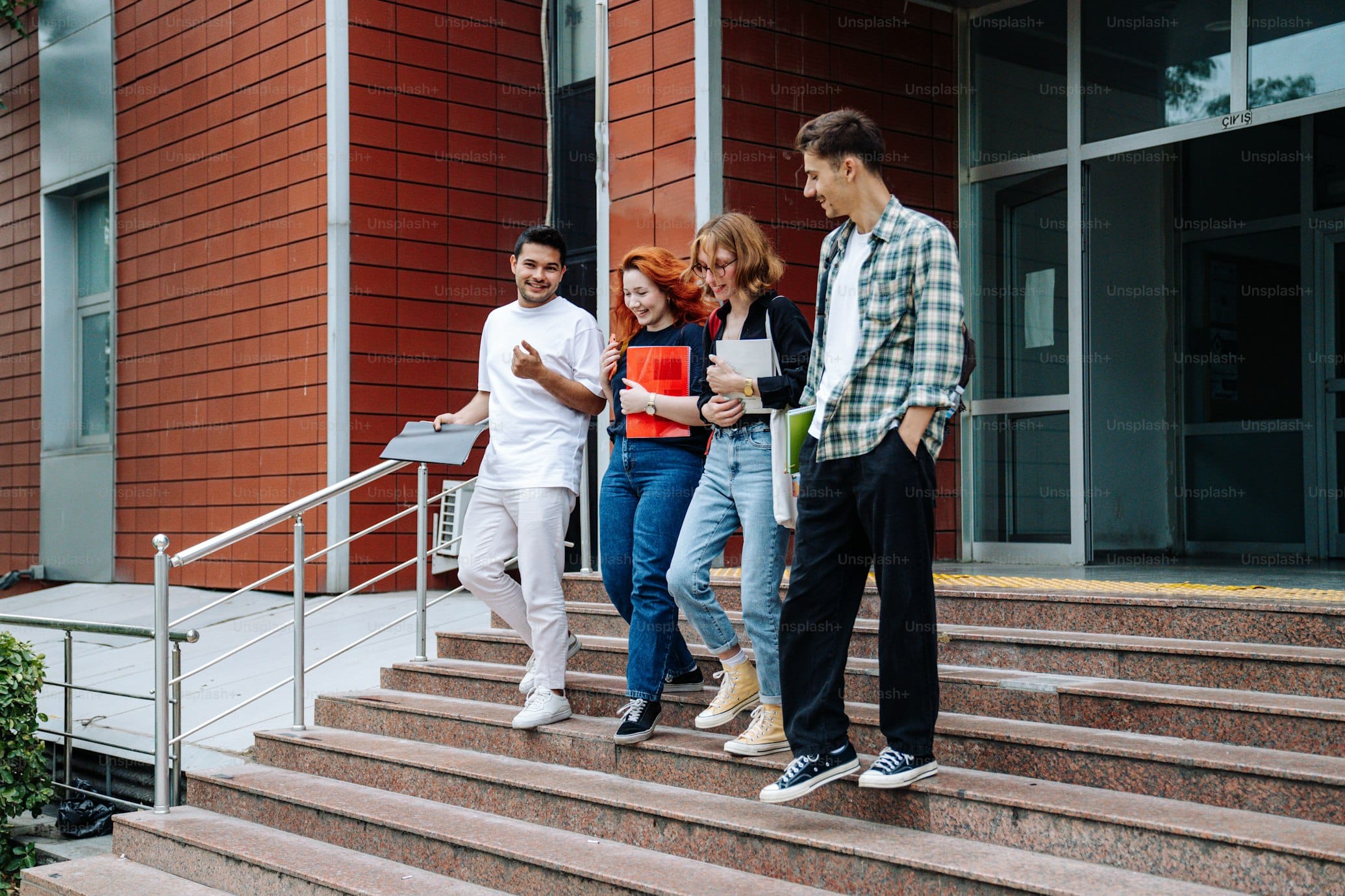 Gruppe junger Menschen verlässt ein Schulgebäude und geht die Treppe hinunter, lächelnd und miteinander sprechend.